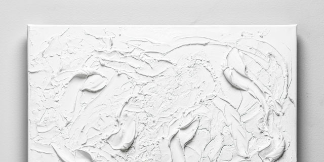 En vit tavla med abstrakt mönster skapat med modeling paste, mot en grå bakgrund.